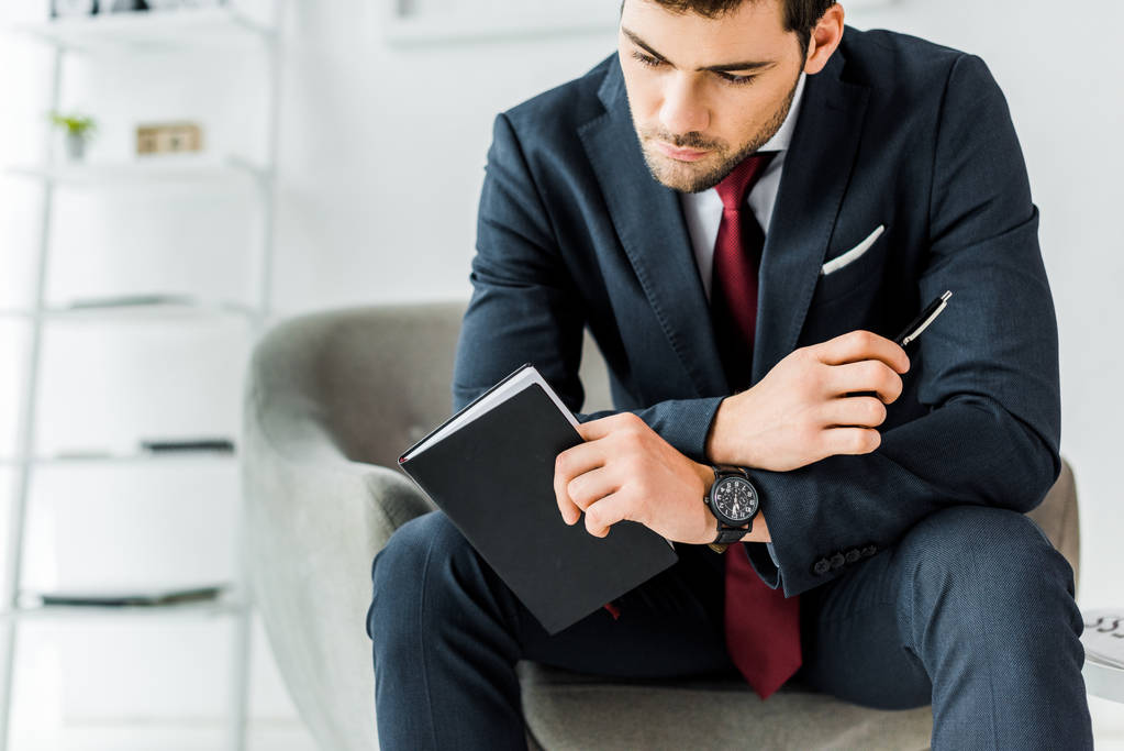 hombre de negocios pensativo en ropa formal sentado y la celebración de cuaderno en la oficina
 - Foto, Imagen