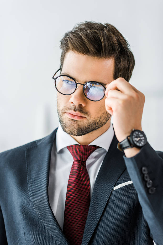 красивый бизнесмен в формальной одежде регулируя очки в офисе
 - Фото, изображение