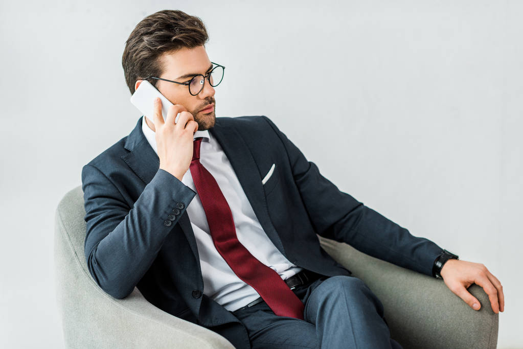 bell'uomo d'affari in abito formale seduto sulla poltrona e che parla su smartphone in ufficio
 - Foto, immagini