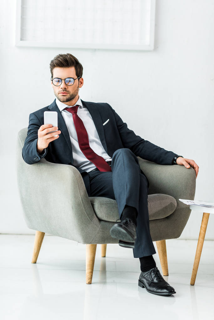 bel homme d'affaires en tenue formelle assis sur un fauteuil et utilisant un smartphone au bureau
 - Photo, image