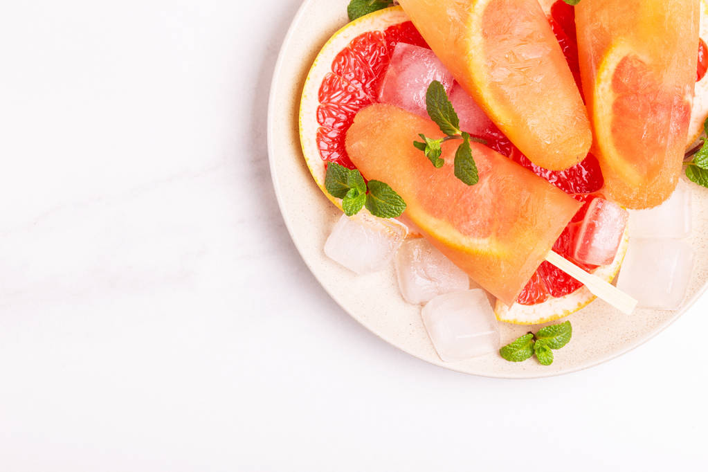 Домашнее грейпфрутовое мороженое со спелыми ломтиками грейпфрута и свежей мятой на светлом мраморном фоне. Здоровые десерты. Мороженое без лактозы
. - Фото, изображение