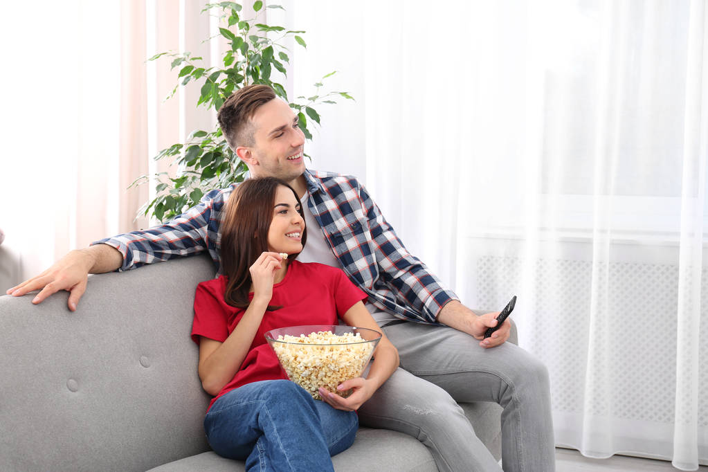 Happy νεαρό ζευγάρι βλέποντας τηλεόραση στον καναπέ στο σπίτι - Φωτογραφία, εικόνα