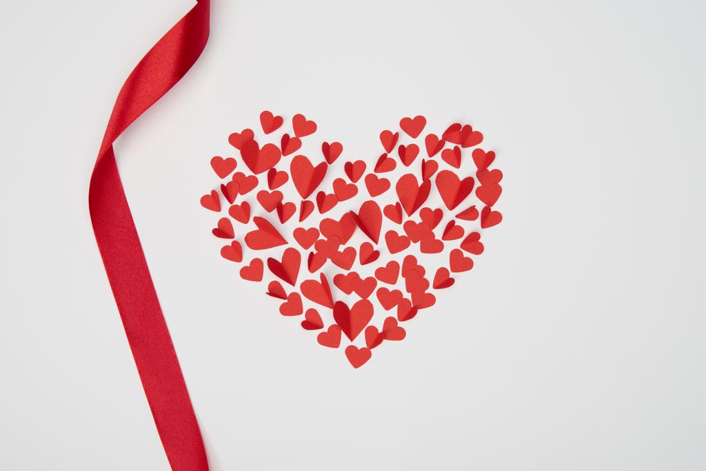 szív alakú kis papír vágott szívét hullámos piros szalaggal, fehér háttér elrendezése - Fotó, kép
