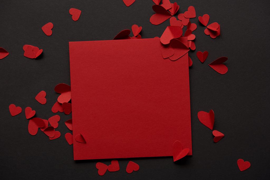 вид зверху на червону порожню листівку і вирізані серця паперу на чорному тлі
 - Фото, зображення