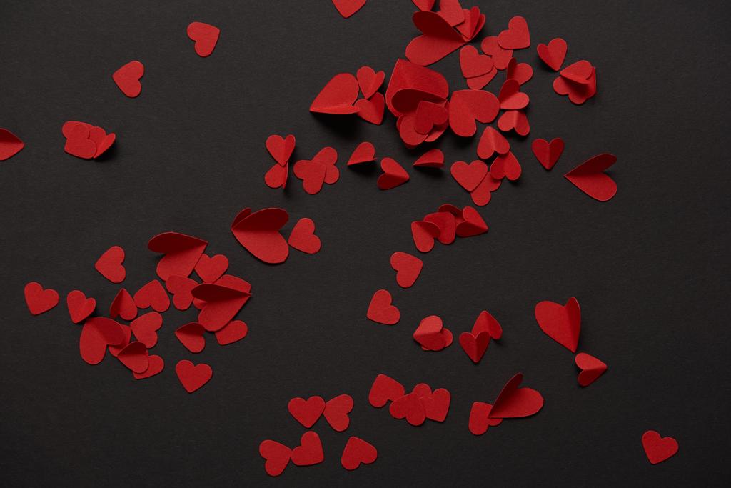 bovenaanzicht van rode kleine papier knippen harten op zwarte achtergrond - Foto, afbeelding
