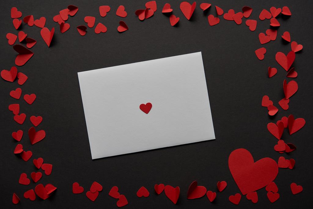 вид зверху на білу вітальну листівку з рамкою з червоного паперу вирізані серця на чорному тлі
 - Фото, зображення
