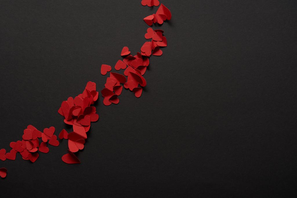 vista superior de los corazones cortados de papel rojo pequeño sobre fondo negro
  - Foto, imagen