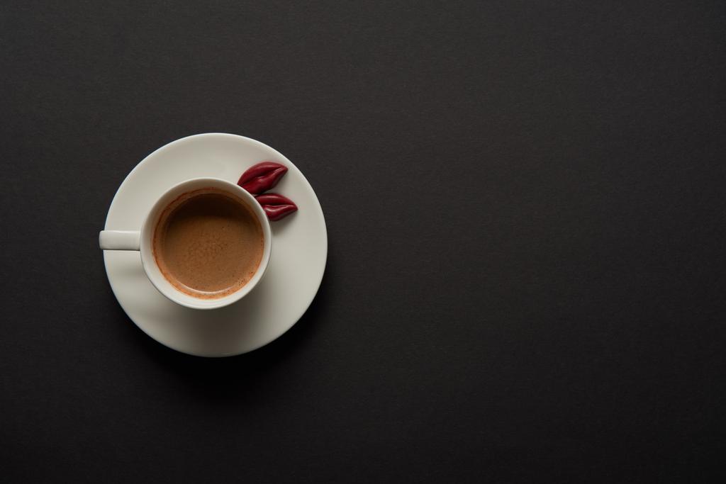 верхний вид чашки кофе с шоколадными губами на блюдце на черном фоне
 - Фото, изображение