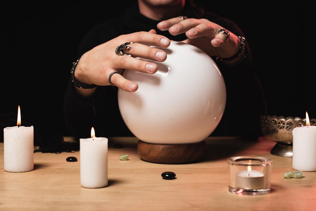 vue recadrée de mains tendues ésotériques au-dessus d'une boule de cristal près de bougies isolées sur noir
  - Photo, image