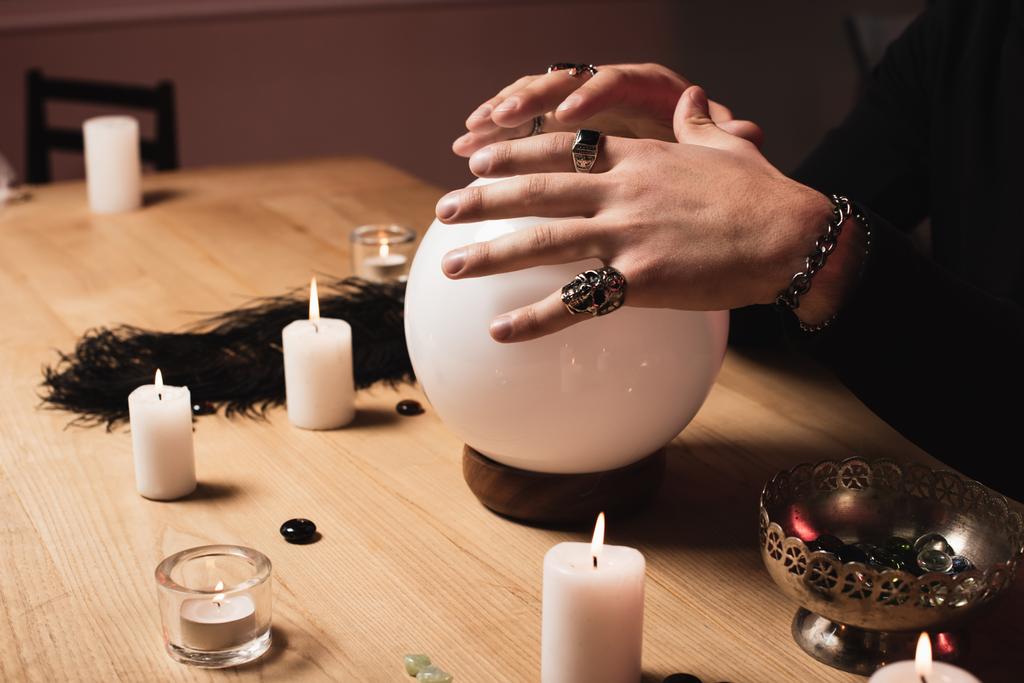Ausgeschnittene Ansicht des psychischen Händchenhaltens über magischer Kristallkugel in der Nähe von Kerzen  - Foto, Bild