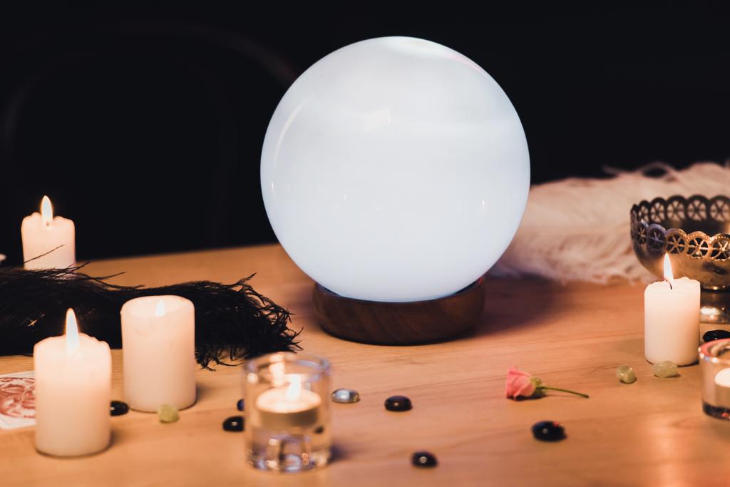 bola de cristal perto de velas e penas em mesa de madeira isolada em preto
  - Foto, Imagem