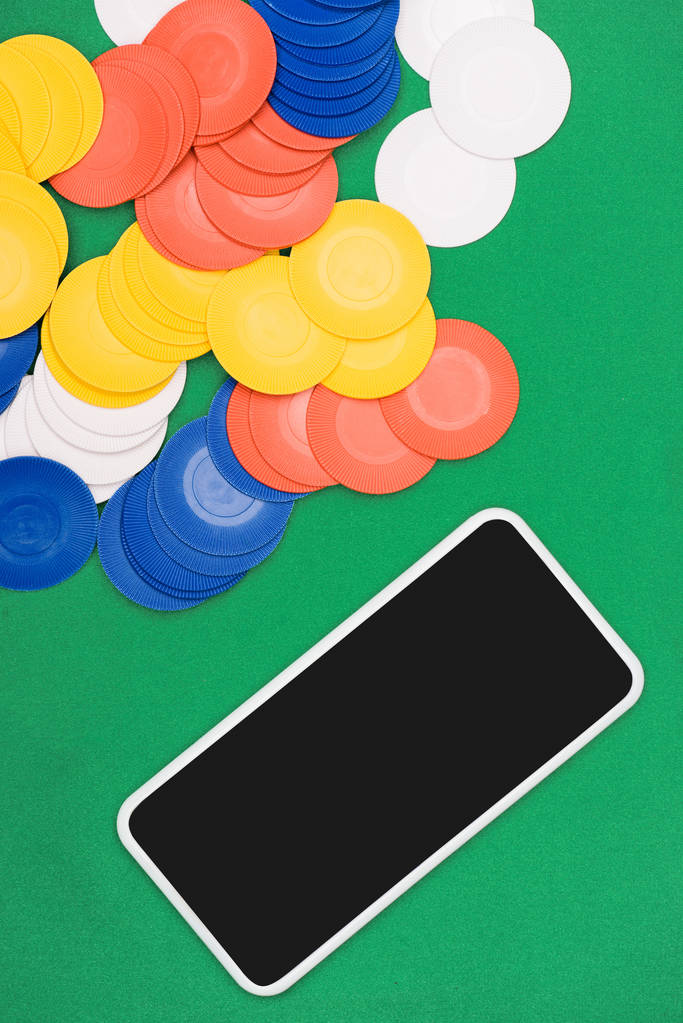 κάτοψη του πράσινου πόκερ τραπέζι με πολύχρωμα κομματάκια και smartphone - Φωτογραφία, εικόνα