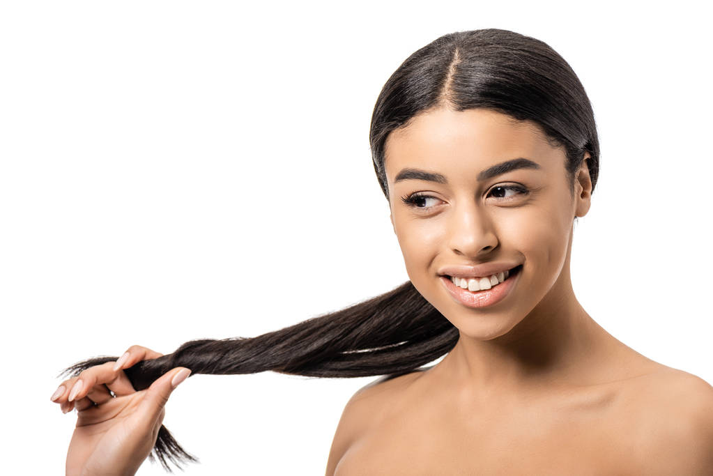 beautiful smiling young african american woman holding long brunette hair and looking away isolated on white - Photo, Image