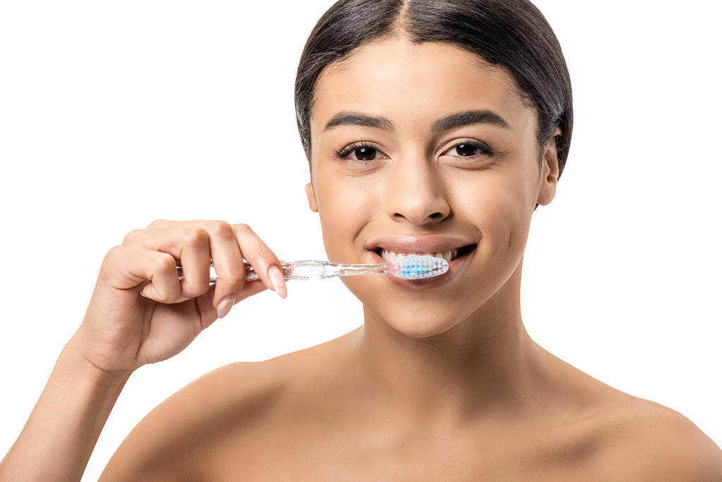 heureuse jeune femme afro-américaine brossant les dents et regardant la caméra isolée sur blanc
 - Photo, image