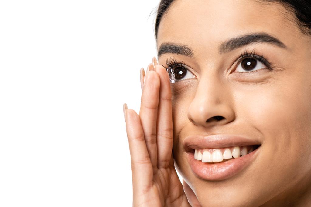 hermosa sonriente joven afroamericana mujer aplicando lentes de contacto y mirando hacia otro lado aislado en blanco
  - Foto, Imagen