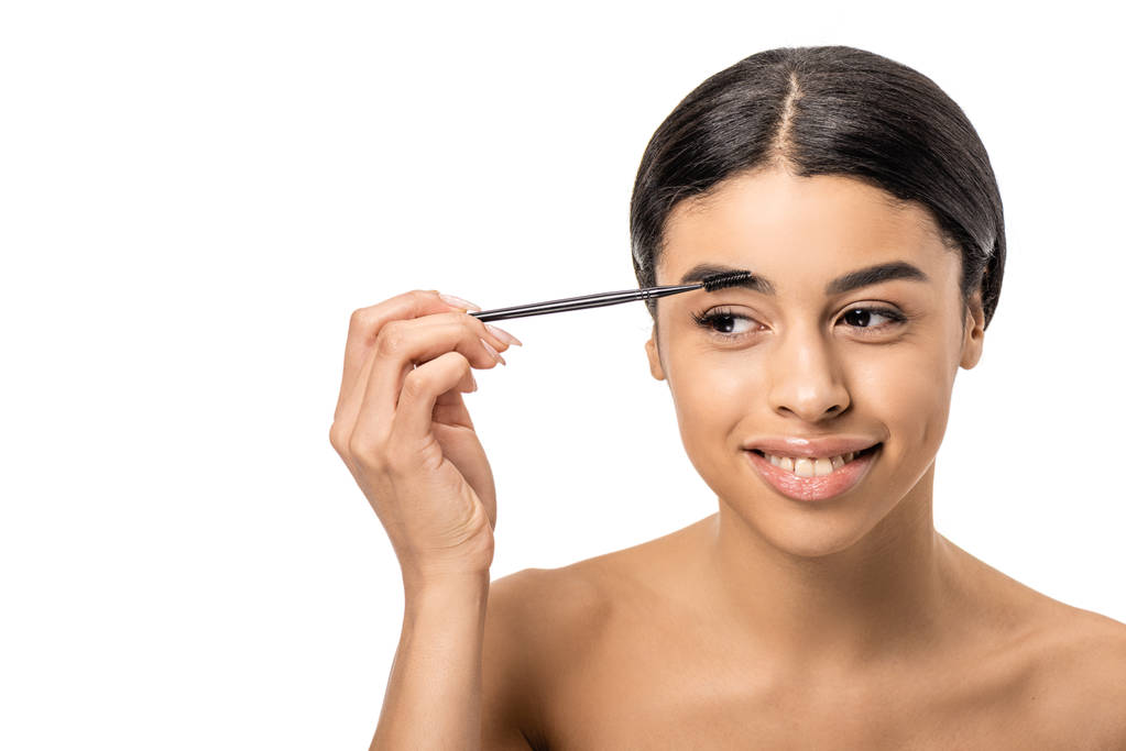 hermosa sonriente afroamericana chica peinando la ceja con cepillo y mirando hacia otro lado aislado en blanco
  - Foto, imagen