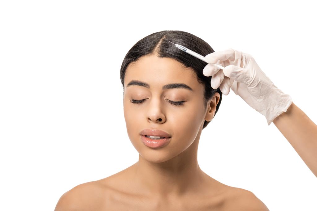 abgeschnittene Aufnahme eines Kosmetikers in Latex-Handschuhen, der jungen afrikanisch-amerikanischen Frau mit geschlossenen Augen eine Schönheitsinjektion gibt, isoliert auf Weiß  - Foto, Bild