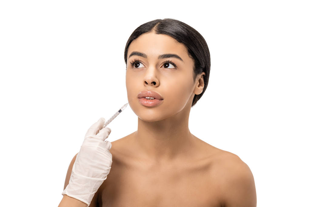 abgeschnittene Aufnahme von Kosmetikerin in Latex-Handschuh, die nackten jungen Afroamerikanerinnen Schönheitsinjektionen gibt, isoliert auf Weiß - Foto, Bild