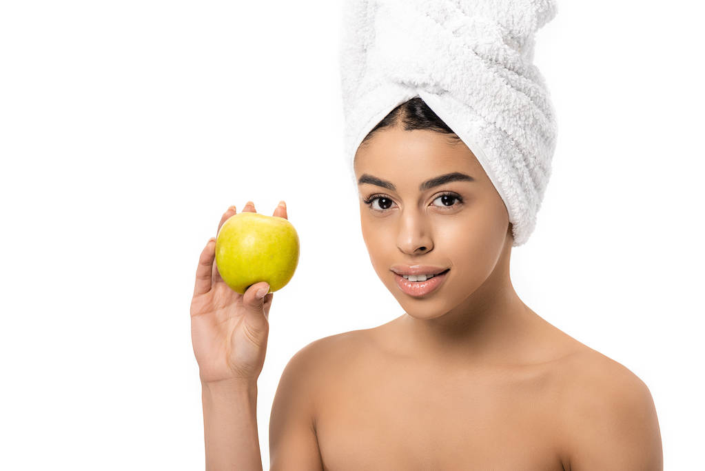 krásná mladá africká americká žena s ručníkem na hlavě drží čerstvé jablko a usmívá se na kameru izolované na bílém - Fotografie, Obrázek