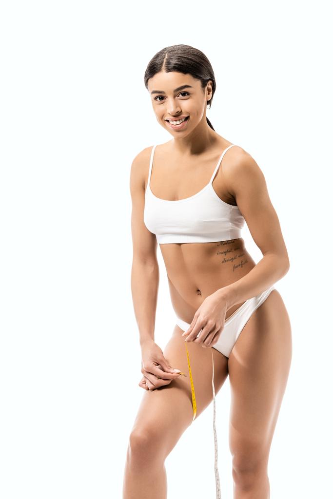 mutlu genç Afro-Amerikan kadın bacak bandı ile ölçme ve üzerinde beyaz izole kamera gülümseyen iç çamaşırı - Fotoğraf, Görsel