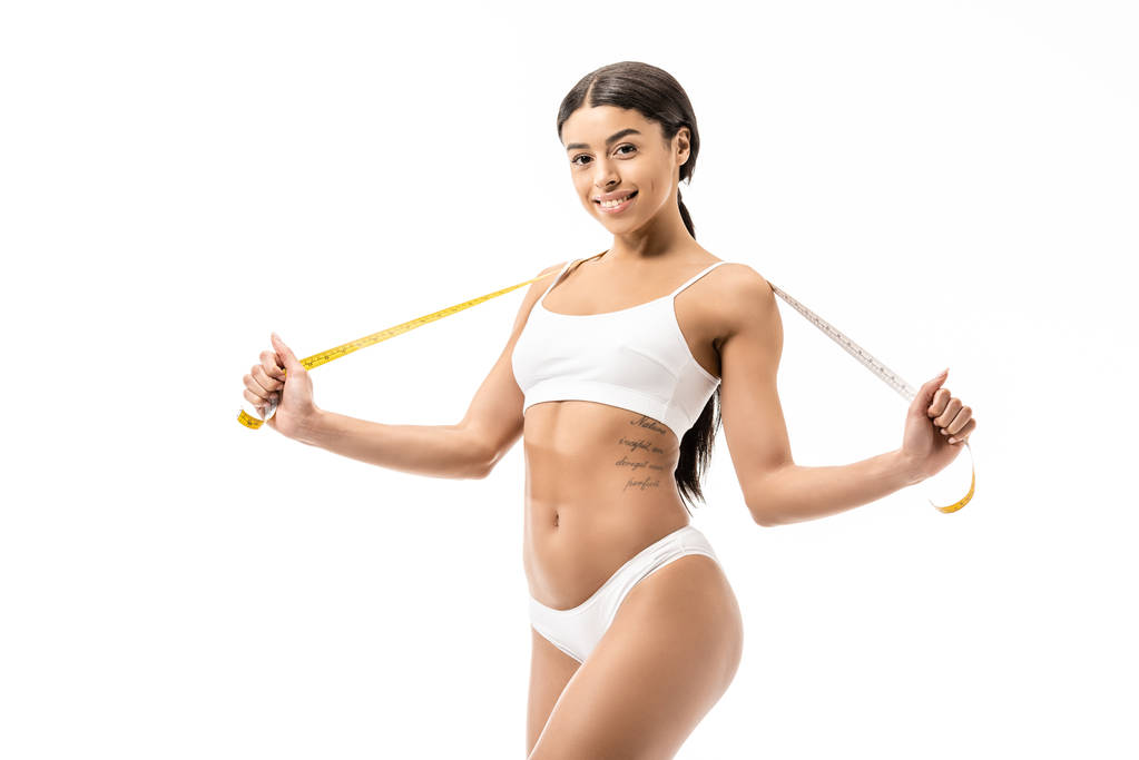 attractive african american girl in underwear holding measuring tape and smiling at camera isolated on white - Photo, Image