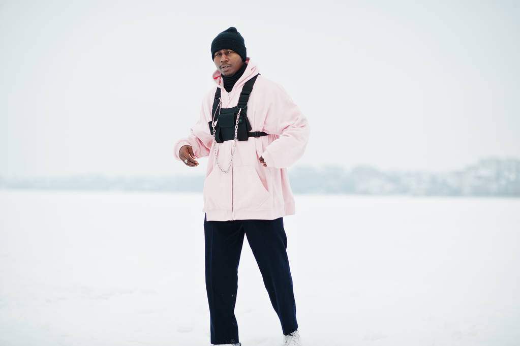 African american człowiek stylowy miejski styl w różowy z kapturem stwarzane na zamarzniętym jeziorze w zimie. - Zdjęcie, obraz