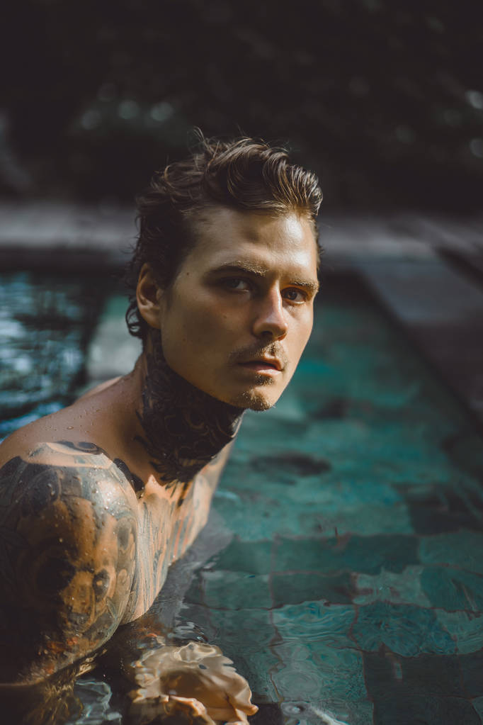 Молодой красивый мужчина в татуировках отдыхает в открытом бассейне. Татуированный человек в бассейне веселится. на бали, индоне
 - Фото, изображение