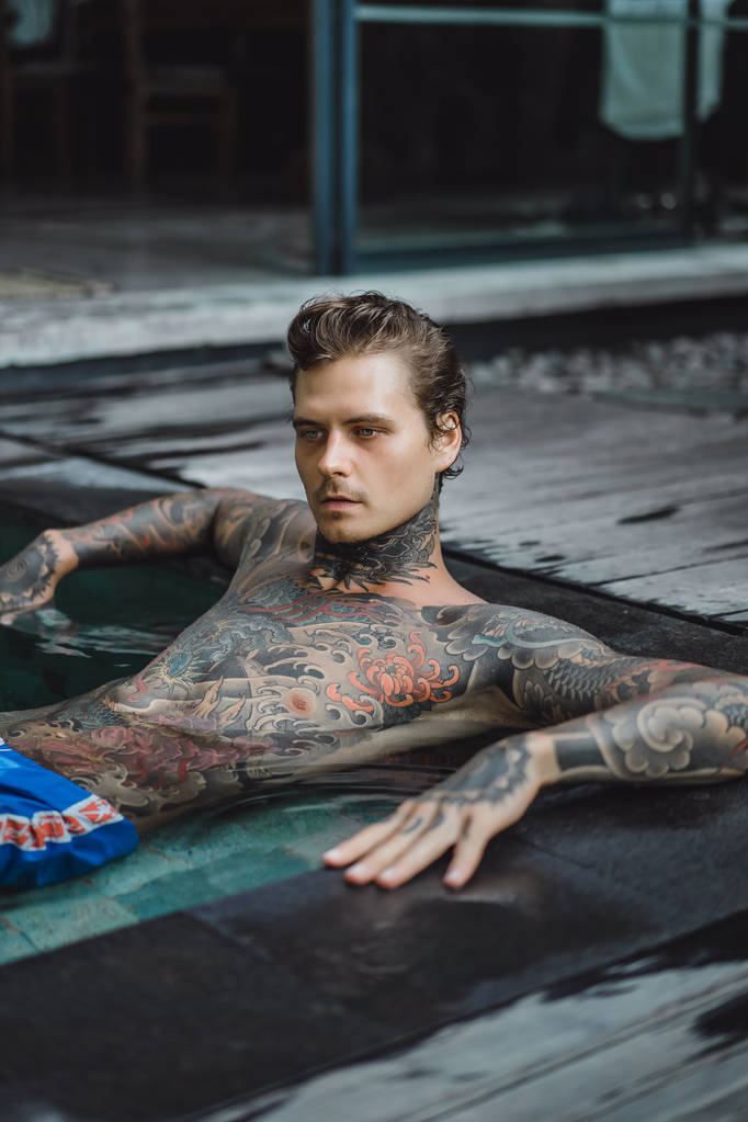 fiatal jóképű férfi tetoválásokat, a szabadtéri medencénél pihen. A tetovált ember a medencében jól szórakozik. a Bali szigetén, Indonézia - Fotó, kép