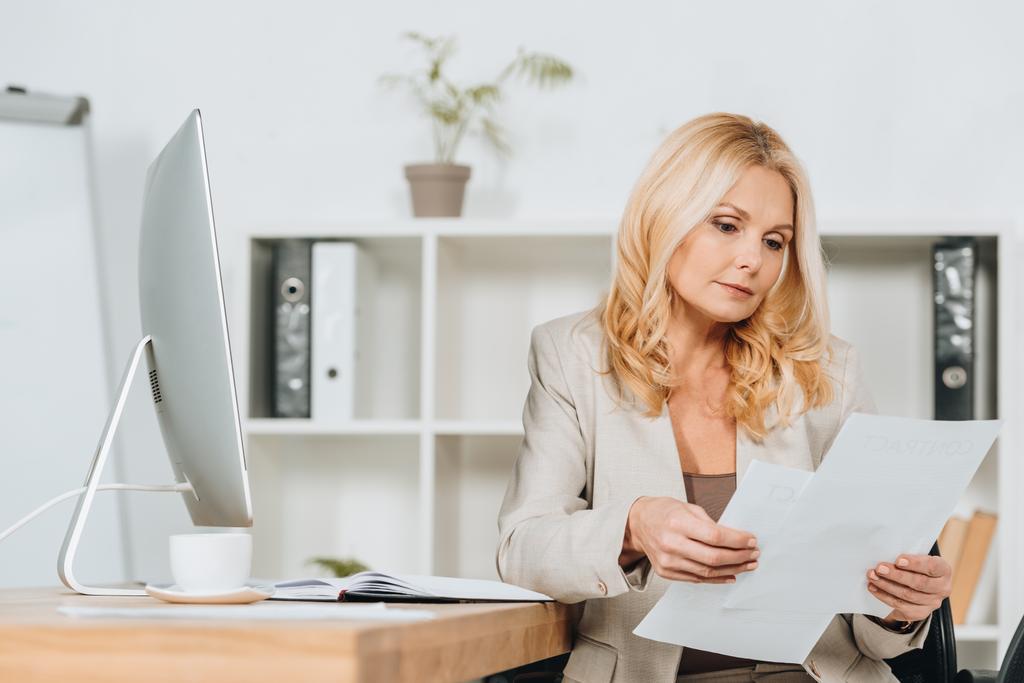 focused mature businesswoman sitting and working with papers in office  - Photo, Image