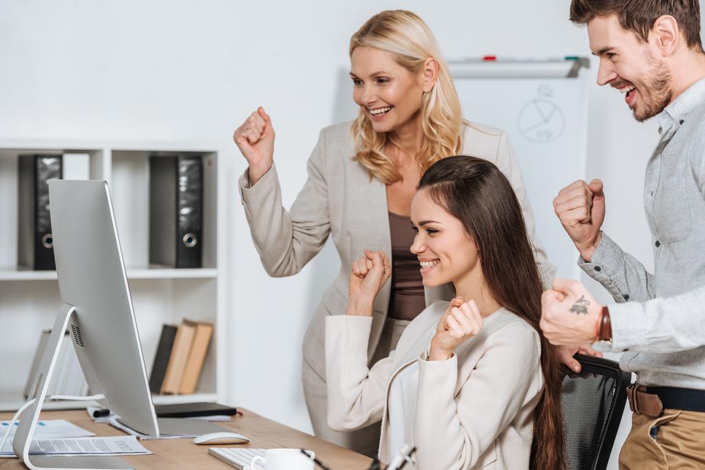 счастливый бизнес-наставник с улыбающимися молодыми коллегами, пожимающими кулаками и смотрящими на настольный компьютер в офисе
   - Фото, изображение