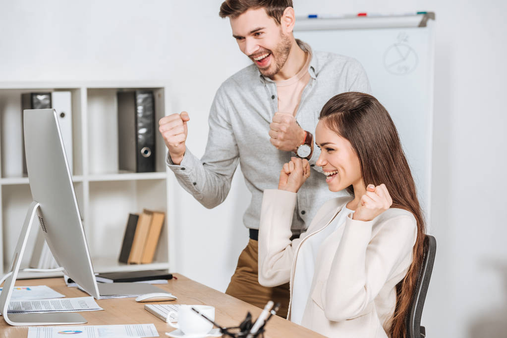 счастливые молодые деловые коллеги трясут кулаками и смотрят на настольный компьютер в офисе
 - Фото, изображение