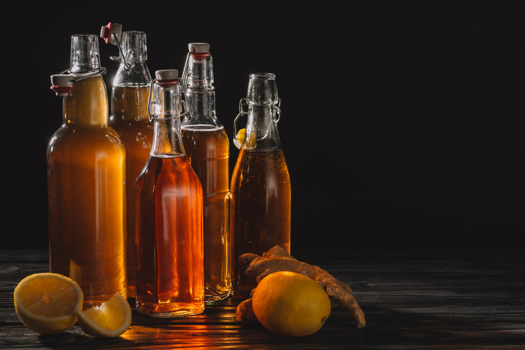σπιτικό βιολογικό τσάι σε γυάλινα μπουκάλια με λεμόνια και ρίζα τζίντζερ που απομονώνονται σε μαύρο - Φωτογραφία, εικόνα