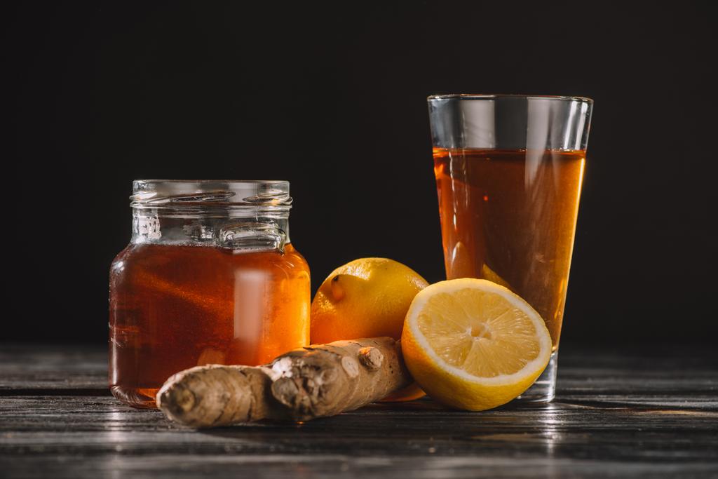 herbata z korzenia imbiru w słoiku i szkło na drewnianym stole na czarnym tle i cytryny - Zdjęcie, obraz