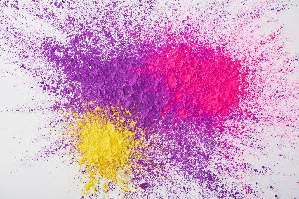 Draufsicht auf Explosion von violettem, rosa und gelbem Holi-Puder auf weißem Hintergrund - Foto, Bild