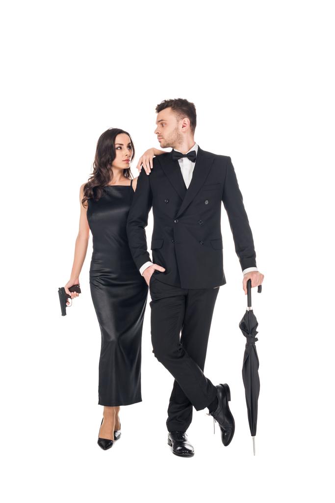 junges elegantes Killer-Paar in schwarzer Kleidung posiert mit Pistole und Regenschirm, isoliert auf weiß - Foto, Bild
