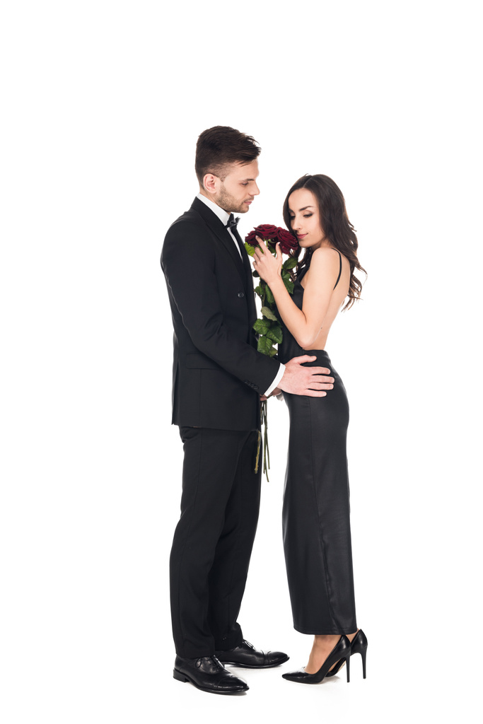 atrakcyjna para elegancki w czarne ubrania pozowanie czerwone róże na Walentynki, na białym tle - Zdjęcie, obraz