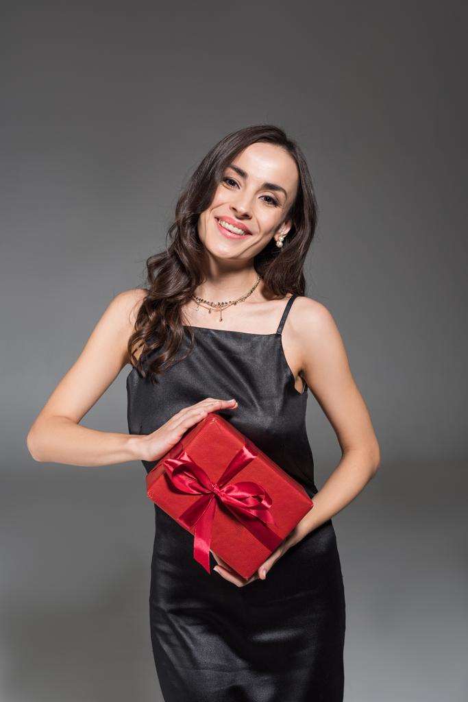 gri izole kırmızı hediye kutusu tutan güzel gülümseyen kadın - Fotoğraf, Görsel