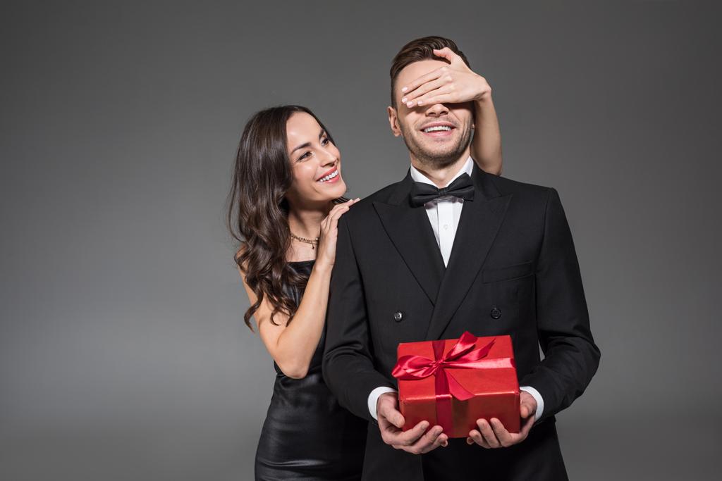 красива жінка закриває очі і робить сюрприз хлопцеві з подарунком на день валентинки, ізольована на сірому
 - Фото, зображення