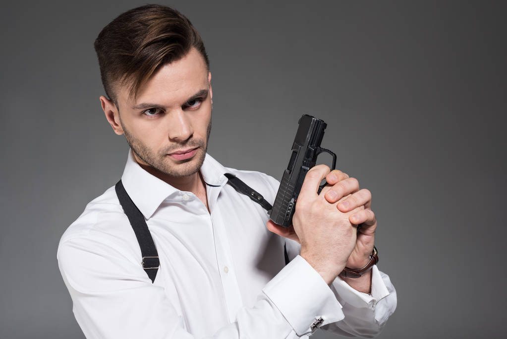 bonito agente secreto com coldre segurando pistola, isolado em cinza
 - Foto, Imagem