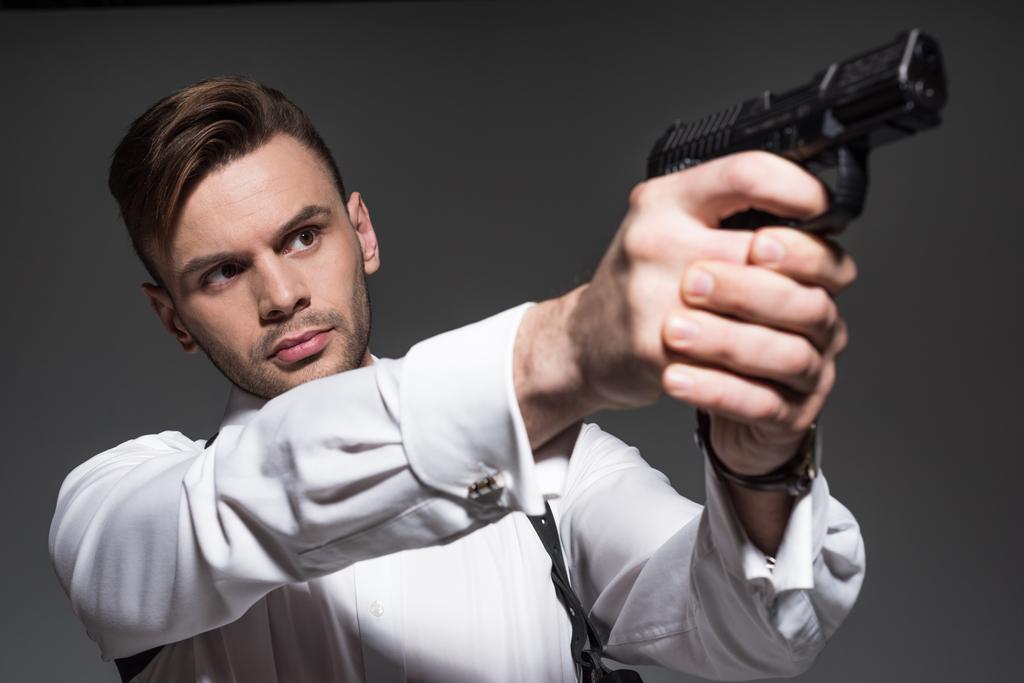 schöner Geheimagent zielt mit Handfeuerwaffe isoliert auf grau - Foto, Bild