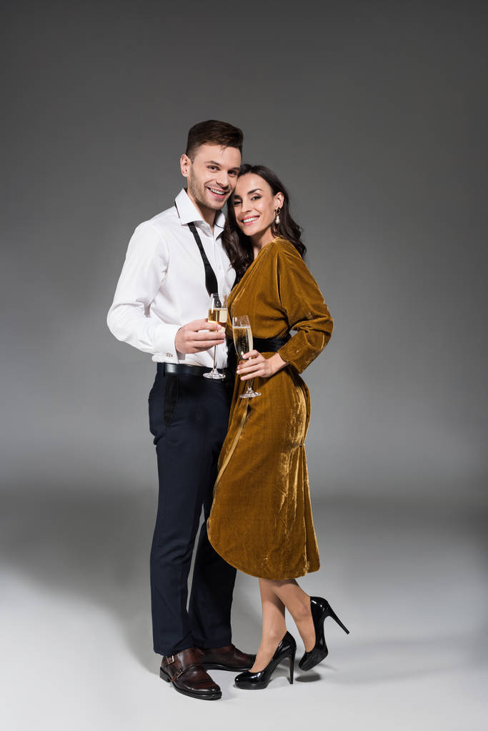 young happy couple hugging and holding champagne glasses on grey - Photo, Image