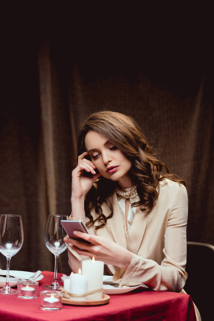 kaunis mietteliäs nainen istuu pöydässä ja käyttää älypuhelinta ravintolassa
 - Valokuva, kuva