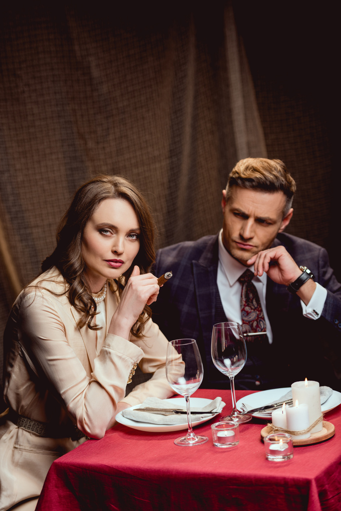 schöne Frau sitzt am Tisch und raucht Zigarre, während sie ein romantisches Abendessen mit einem schönen Mann im Restaurant einnimmt - Foto, Bild