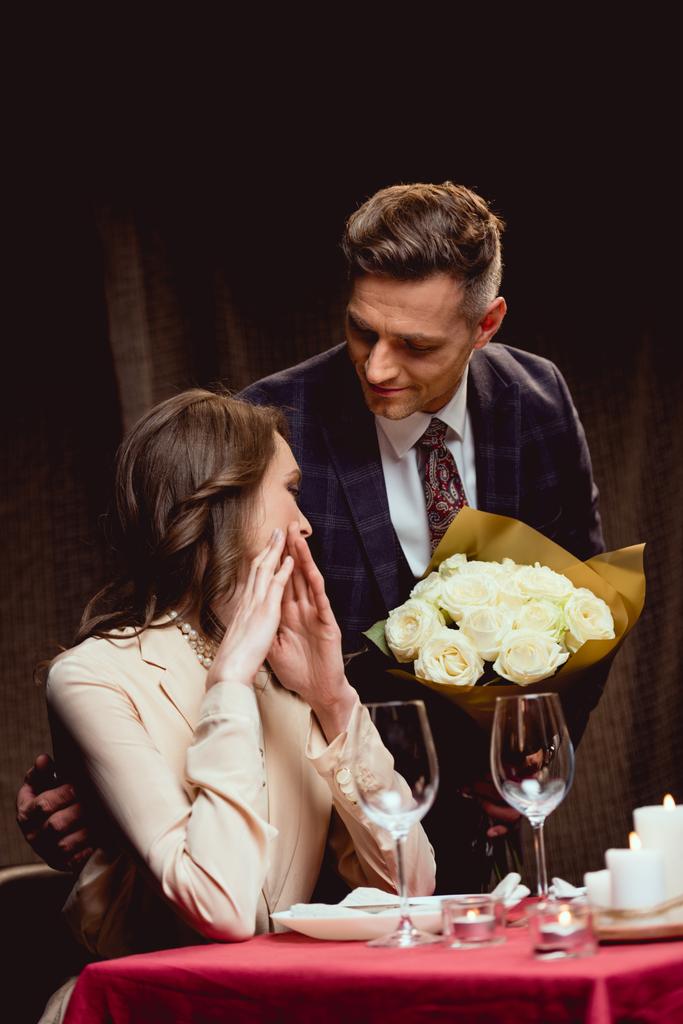 ο άνθρωπος παρουσιάζει λουλούδια έκπληκτος γυναίκα κατά τη διάρκεια της ρομαντική ημερομηνία στο εστιατόριο - Φωτογραφία, εικόνα