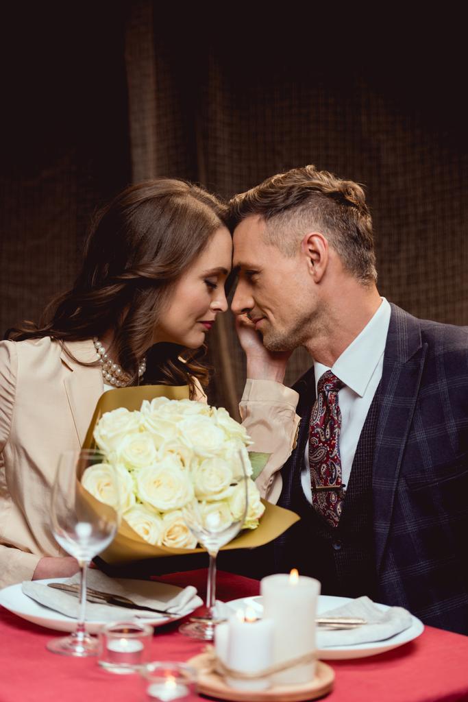 gyönyörű pár, a csokor virág asztalnál ült és nézett minden más romantikus dátum alatt az étteremben - Fotó, kép