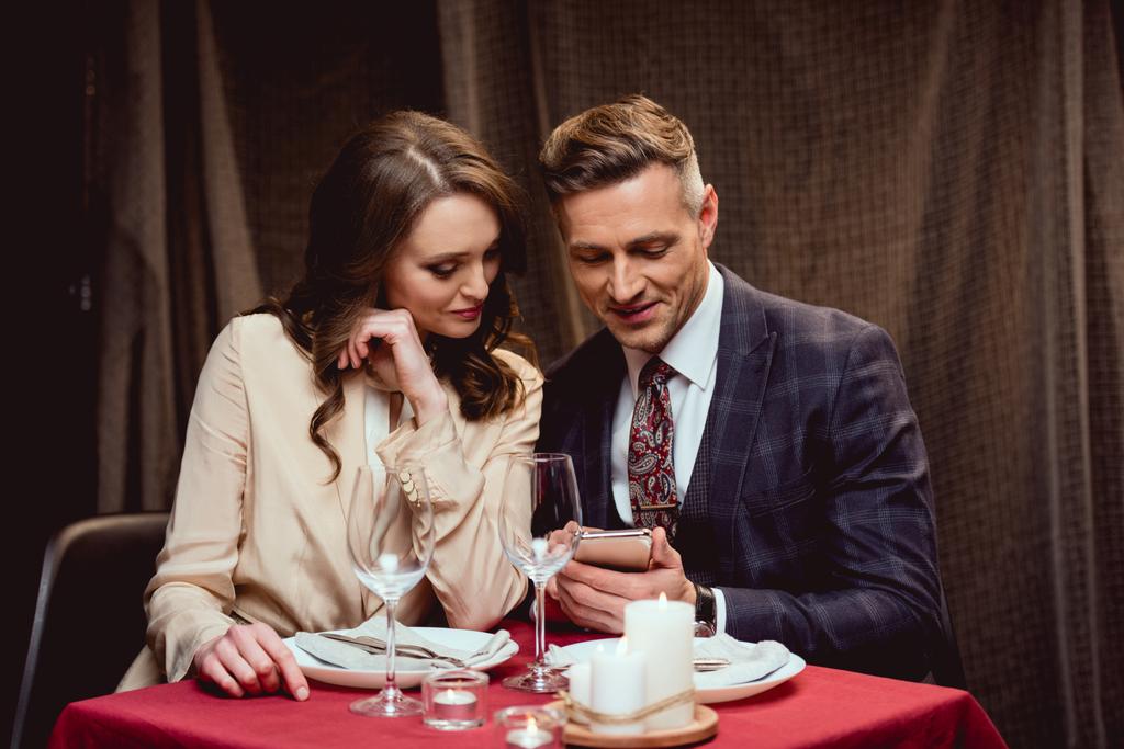 Paar sitzt bei romantischem Date im Restaurant am Tisch und nutzt Smartphone - Foto, Bild