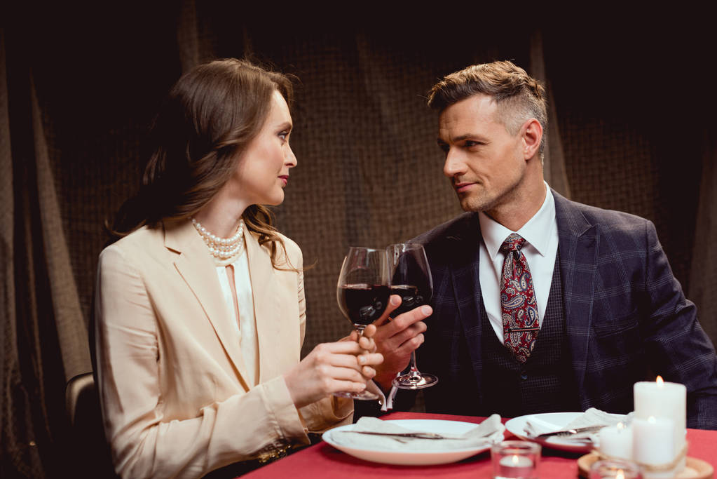 pareja sentada en la mesa y tintineo vasos de vino tinto durante la cita romántica en el restaurante
 - Foto, Imagen
