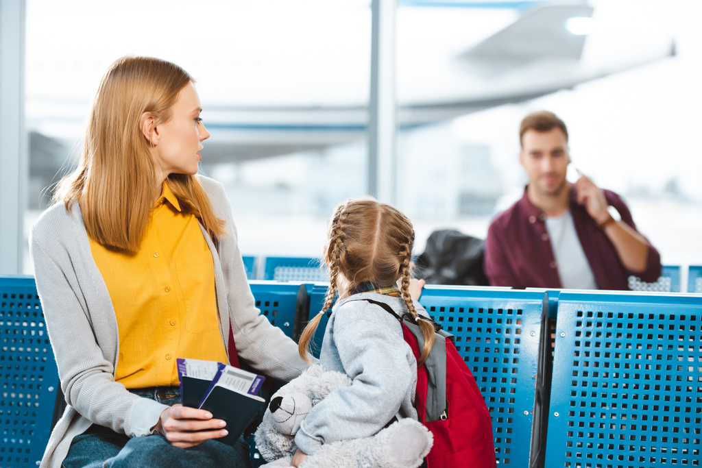 foco seletivo da mãe segurando passaportes com passagens aéreas perto da filha e olhando para o homem no aeroporto
  - Foto, Imagem