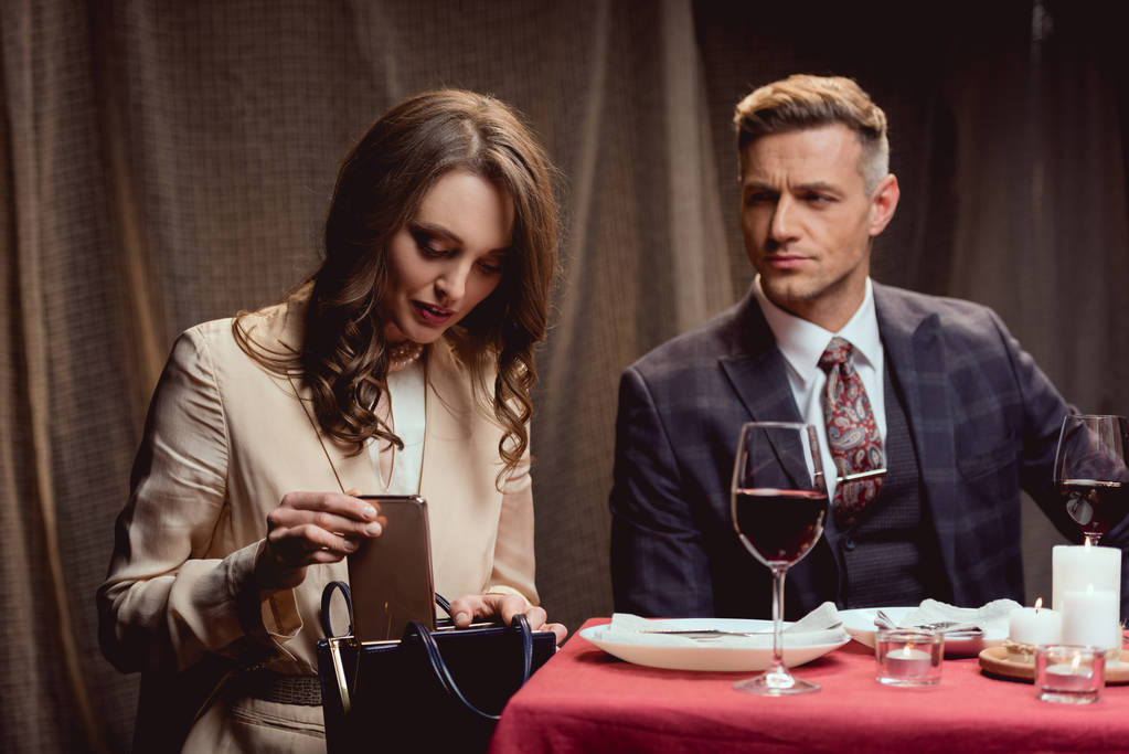 hombre guapo mirando a la mujer poner teléfono inteligente en el bolso durante la cita romántica en el restaurante
 - Foto, imagen