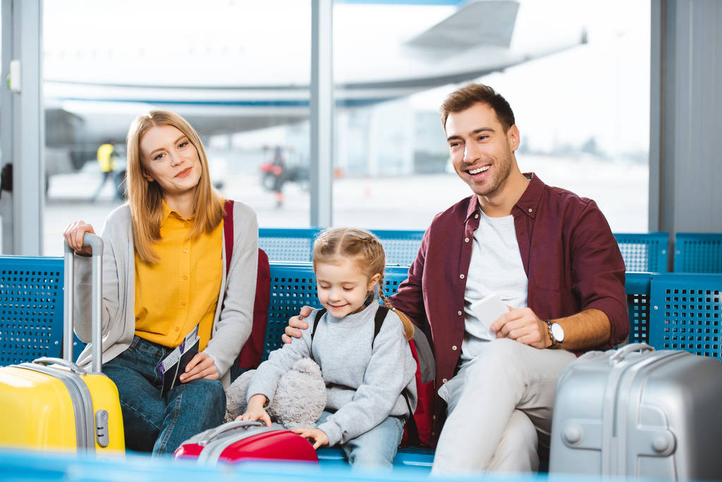 famille heureuse attendant dans le salon de départ et souriant près des bagages
  - Photo, image